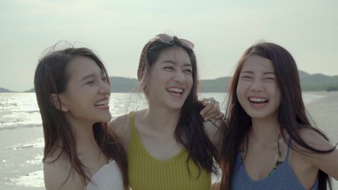 Three asian girl friends are smiling, greeting and enjoying with camera for video calling in evening on summer sea beach. Girl friends having fun at the sea and beach. Youth and happiness concept.