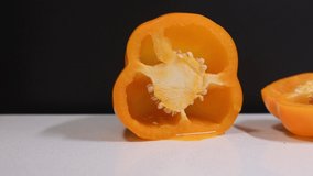 Video close up cutting orange bell pepper into small pieces. Preparing pepper for cooking. 4K video of vegetable. Dark background and white chopping board.