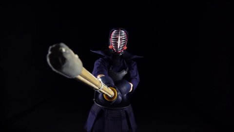 Masculine Kendo warrior practicing martial art with the bamboo bokken on black background. Slow motion