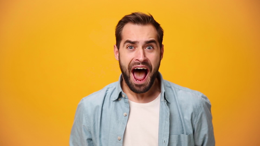 Handsome unshaven bearded young guy 20s in denim shirt white t-shirt isolated over yellow background in studio. People sincere emotion lifestyle concept. Looking at the camera scream win enjoy delight | Shutterstock HD Video #1042986751