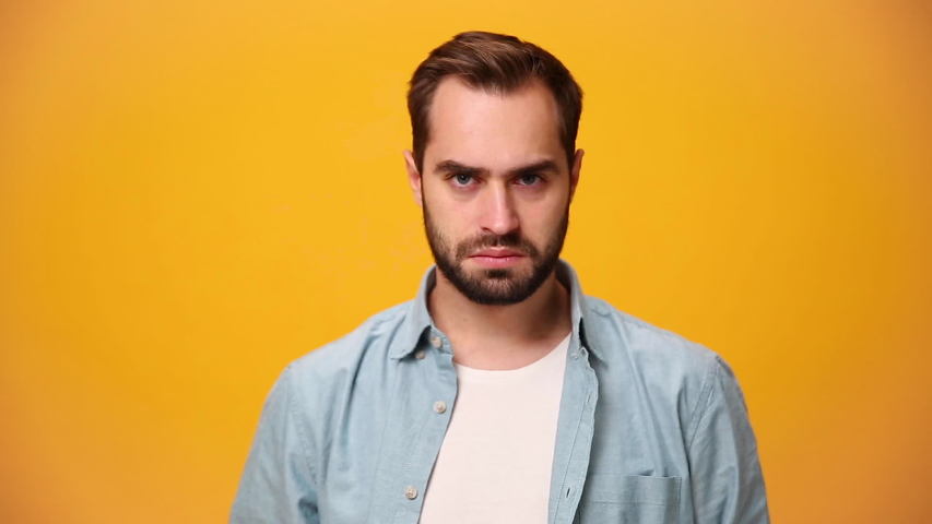 Angry swearing unshaven bearded young guy 20s in denim shirt white t-shirt isolated over yellow background in studio. People sincere emotions, lifestyle concept. Looking at the camera scream and shout Royalty-Free Stock Footage #1042986865