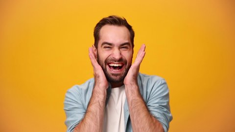Handsome unshaven bearded young guy 20s in denim shirt white t-shirt isolated over yellow background in studio. People sincere emotions, lifestyle concept. Looking at camera scream rejoice win happy
