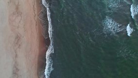 Aerial view of a low key A video about a tropical beach at blue hour after sunset showing evening footage of green foaming ocean waves crashing onto the coastline. Top view without people