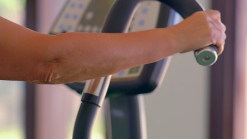 Woman doing a cardiovascular workout in a gym in a close up on her hand on the handlebar of the machine and the digital readout