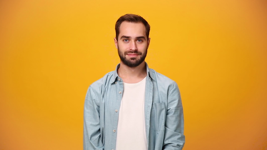 Handsome smiling bearded young guy 20s in denim shirt white t-shirt isolated on yellow background in studio. People sincere emotions, lifestyle concept. Looking approvingly at camera showing thumbs up Royalty-Free Stock Footage #1042994590