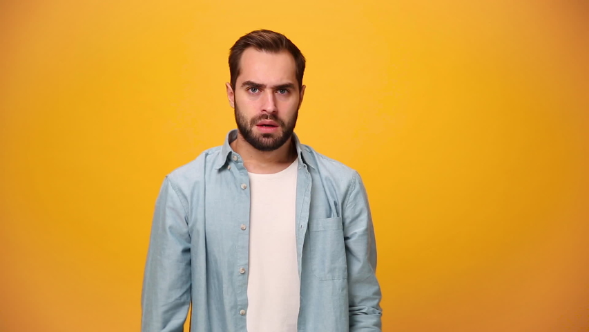 Angry bearded young guy 20s in denim shirt white t-shirt isolated over yellow background in studio. People sincere emotions, lifestyle concept. Looking at the camera. Covering ears with fingers scream Royalty-Free Stock Footage #1042995109