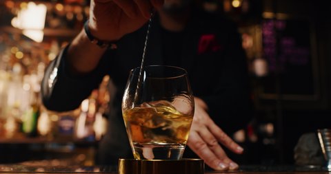 Close up of a professional bartender is mixing an alcoholic cocktail with professional crystal long lasting ice cubes to customers at the bar or disco club.