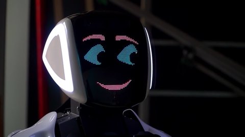 The robot shows emotions. Artificial Intelligence. Modern robotics. The robot looks and smiles at people. Eyes of the robot. Cyborg. The robot is looking at the camera at a person. smart computer