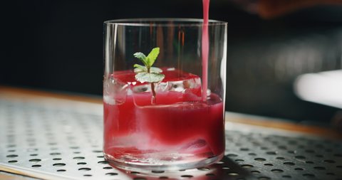 Close up of a professional bartender is preparing an alcoholic cocktail with professional crystal long lasting ice cube with mint inside to customers at the bar or disco club.