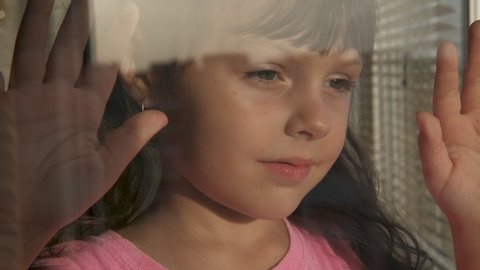 Portrait of a child looking out the window. Beautiful little girl looks at the sunset through the window.