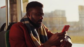 Attractive african young businessman wearing autumn outfit using a smartphone device driving in public transport admiring bright sunrise behind a window. - Powered by Shutterstock - Get 15% off with code: PIKWIZARD15