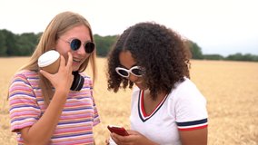 Slow motion video clip of pretty blonde girl and mixed race teenager young women wearing sunglasses drinking coffee and taking selfies on their smart phones for social media