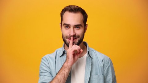 Handsome guy 20s in denim shirt white t-shirt isolated over yellow background in studio. People sincere emotions, lifestyle concept. Look at camera say hush be quiet with finger on lips shhh gesture.