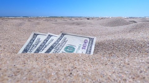 Money dolars half covered with sand lie on beach close-up. Money grows out of the ground. Dollar bills partially buried in sand on sea ocean beach Concept finance money holiday relax vacation.