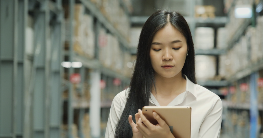 Beautiful business woman using tablet for choose product in a large industrial room of a furniture warehouse.