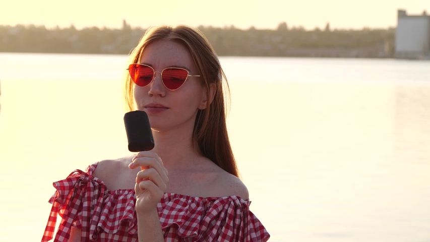 Beautiful young woman eating ice cream outdoors at sunset. Slow motion effect