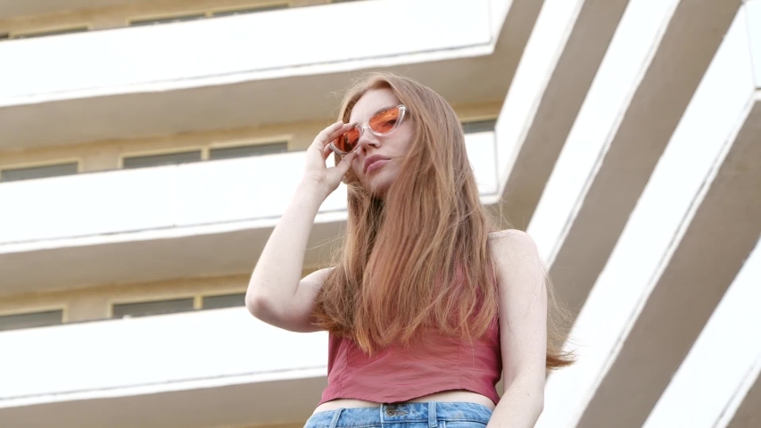 Beautiful young woman near modern building, low angle view. Slow motion effect