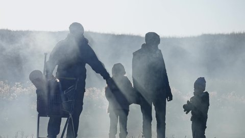 Silhouettes of survivor family in gas mask standing through clouds of toxic smoke and cinder in empty dead landscape.