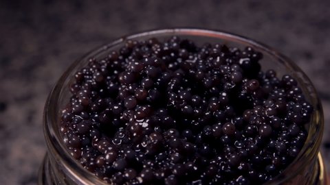 Close-up of a spoon taking a black caviar from a glass jar 