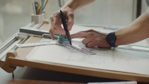Architect's desk: drawings, tape measure, ruler and other drawing tools. Engineer works with drawings in a bright office, close-up. Insturments and office for designer. Male hands draw with a pencil