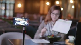 healthy food, a young beautiful blogger talks about a fashionable diet, writes videos for his vlog on a smartphone sitting at a table in a cafe, people and blogs