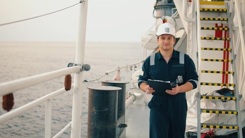 Marine chief officer or chief mate on deck of ship or vessel. He fills up ahts vessel checklist. Ship routine paperwork. He holds VHF walkie-talkie radio in hands.