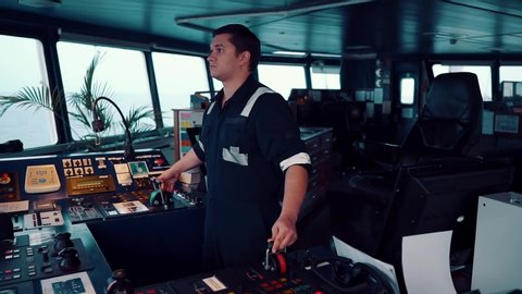 Marine navigational officer during navigational watch on Bridge . He is maneuvering the ship. Work at sea.