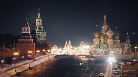 Beautiful panorama of Moscow Red Square on a calm winter night with the Kremlin clock tower, the Cathedral of Vasily the Blessed and brightly illuminated GUM. Rare cars and pedestrians passing by.