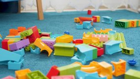 Closeup dolly video of messy floor at childs room at house. Colorful bricks and building blocks lying on blue carpet at playroom