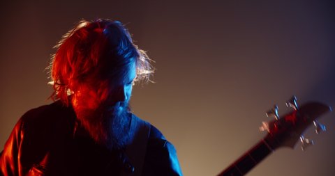 An amazing rock music player performing. Grunge musician is playing rock on bass guitar on stage, making a cool solo in red and blue neon lights 4k footage