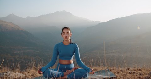 Athletic girl meditating during sunrise. Fit girl training in mountains, sitting in lotus yoga pose - healthy way of life, zennism concept 4k footage