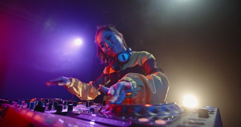 Asian female dj is rocking the party up, creating a mix at turntables in nightclub red and blue lights - nightlife, dance music concept 4k footage