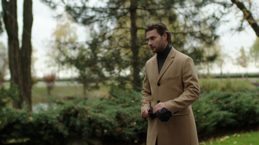 A confident handsome guy is walking through an autumn park to a business meeting. Stylishly dressed man under a black umbrella.