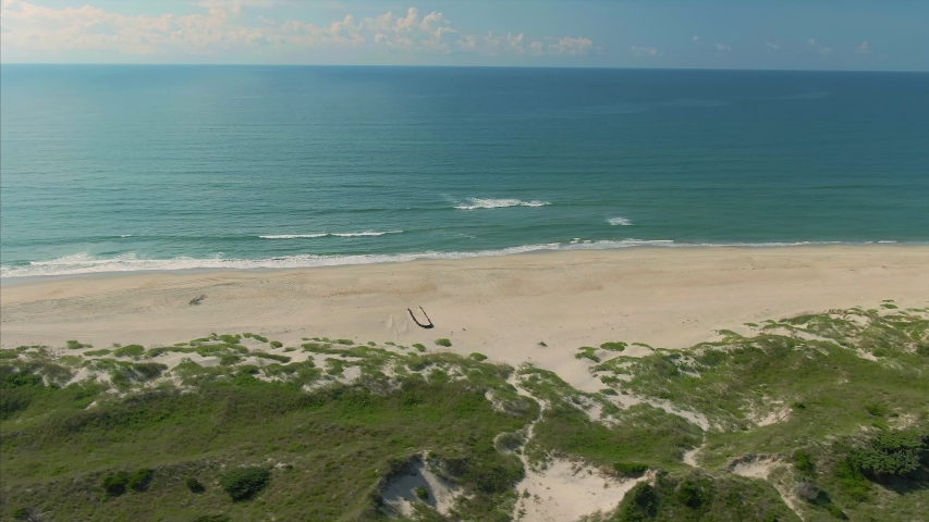 Aerial: Sandy coastline & sanddunes of the Outer banks. A highway runs the length of the beach. Ocracoke, North Carolina, USA. 