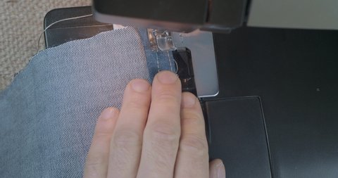 Close-Up Man's Hand Sewing With Denim Jeans On A Sewing Machine. Alteration Jeans, Hemming A Pair Of Jeans, Handmade Garment Industrial Concept. Cinema 4k Video. C4K