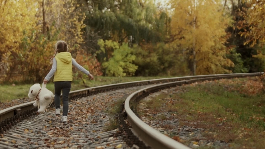 Lonely little girl with a Teddy bear on her shoulders is on the railway