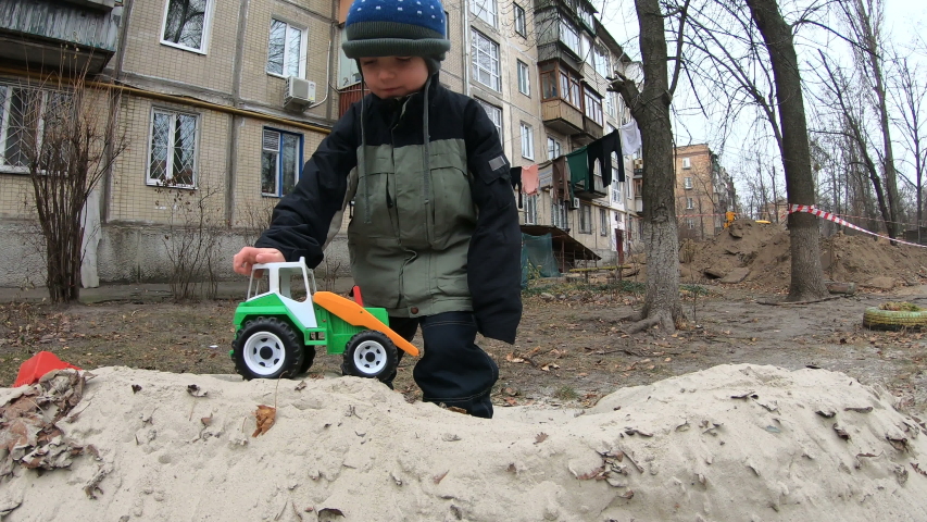 Little boy in a hat and autumn jacket plays on the street with a toy tractor