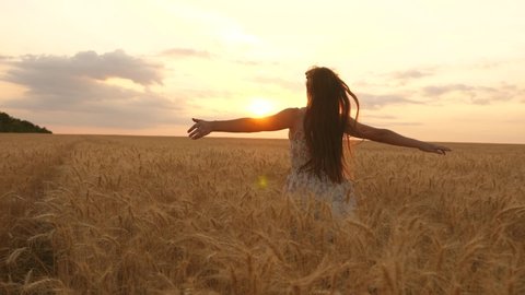 happy young girl runs in slow motion across field, touching ears of wheat with her hand. Beautiful free woman enjoying nature in warm sunshine in a wheat field on sunset background. girl travels.