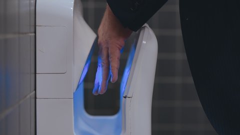 Business man in formal suit and white shirt is using hand dryer in a public toilet or lavatory after washing hands