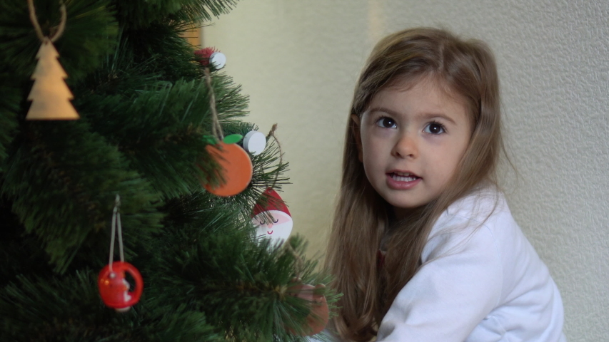 Boxing Day. Christmas gift opening. Little girl beneath Christmas tree looking for presents. Happy childhood. Perfect cinematic girl aged four. Portrait of ceiling caucasian child. 