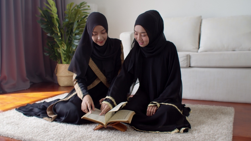 4K Locked shot the pretty young Muslim woman and her girl friend wearing beige hijab and traditional clothes sitting on carpet, They are talking while learning about the Quran or holy book of Islam
