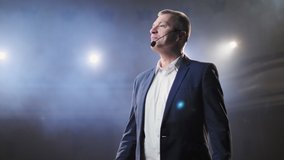 Portrait of men speaking through a microphone in dark conference hall. Man talks into microphones at press conference. Profile of mature male politician speaking passionately from tribune - Powered by Shutterstock - Get 15% off with code: PIKWIZARD15