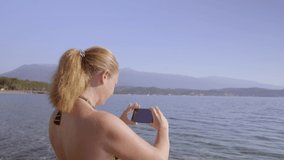 Happy female tourist shoots sea using phone.