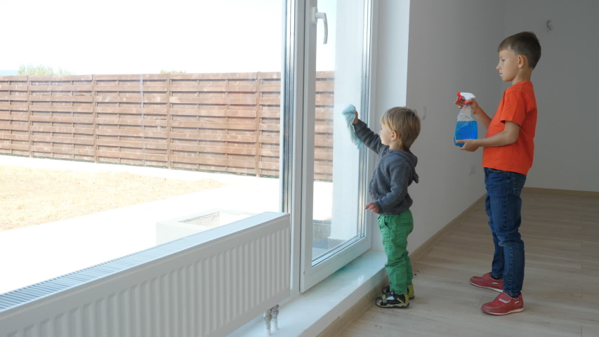 Two brothers working together, bigger boy spray with detergent, toddler child cleaning window, real family teamwork