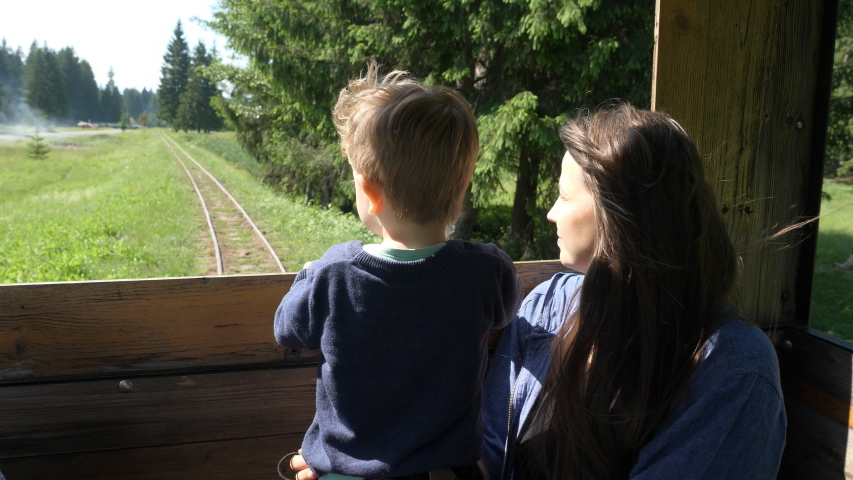 Young beautiful mother and little child looking out open train window, travel