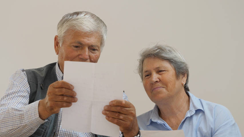 Happy old couple of old man and woman reading a letter, interesting news from family
