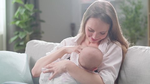 Mom breastfeeds her little daughter in the morning sun in the living room