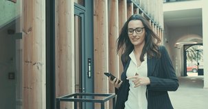 Attractive business woman with eye glasses smiling portrait. Young business people confident pretty. Female goes with smartphone in the city. Growing, success. 4K slow motion video