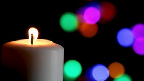 Large white candle shines its candlelight in the dark with festive colorful lights in the soft-focused background of this seamless loop. Great for Christmas or any birthday party or celebration!