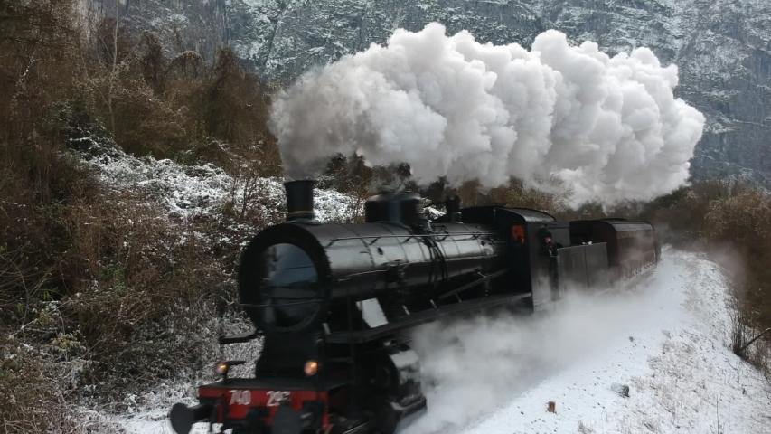 Historic steam train rolling through the snowy valley in a winter day
